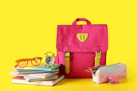 Pink school backpack with different stationery, eyeglasses and alarm clock on Stock Photos
