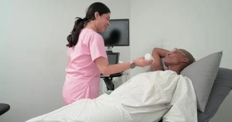 Pink-scrub tech scanning African-American woman neck for exam with probe gel in Stock Footage 336483969