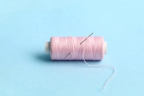 Pink sewing thread with needle on blue background Stock Photos