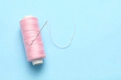 Pink sewing thread with needle on blue background Stock Photos