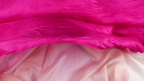 Pink silk fabric falls smoothly in slow motion onto bright textiles.  Stock-Footage 337405419