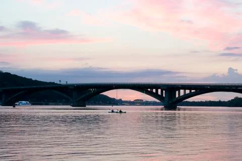 Pink sky at sunset. Kayaks float on the river on the evening bridge Foto stock