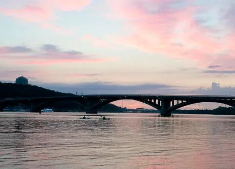 Pink sky at sunset. Kayaks float on the river on the evening bridge Stock Photos