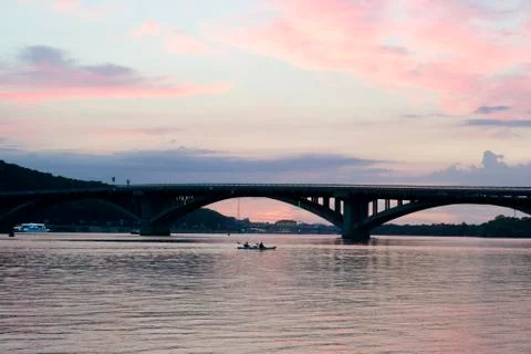 Pink sky at sunset. Kayaks float on the river on the evening bridge Stock Photos