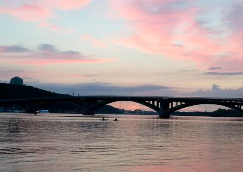 Pink sky at sunset. Kayaks float on the river on the evening bridge Stock Photos
