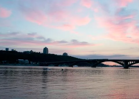 Pink sky at sunset. Kayaks float on the river on the evening bridge Stock Photos