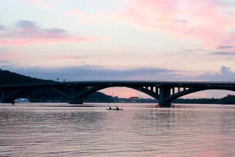 Pink sky at sunset. Kayaks float on the river on the evening bridge Stock Photos