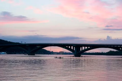 Pink sky at sunset. Kayaks float on the river on the evening bridge Stock Photos