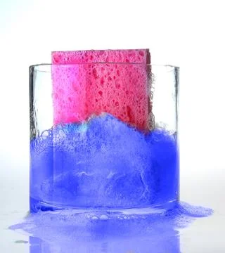 Pink Sponge falling into Blue colored Soapy Water in Glass Bowl Stock Photos