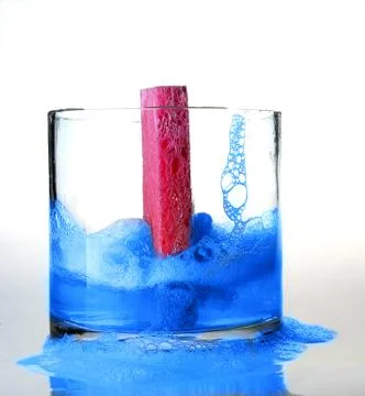 Pink Sponge falling into Blue colored Soapy Water in Glass Bowl Foto stock