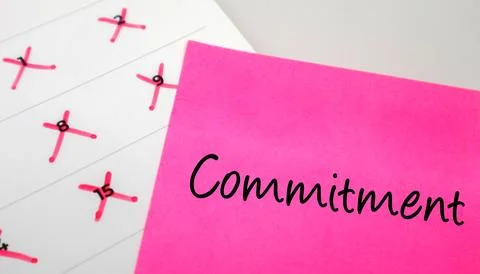Pink sticky note with Commitment text on a calendar with red marked dates. .. Stock Photos