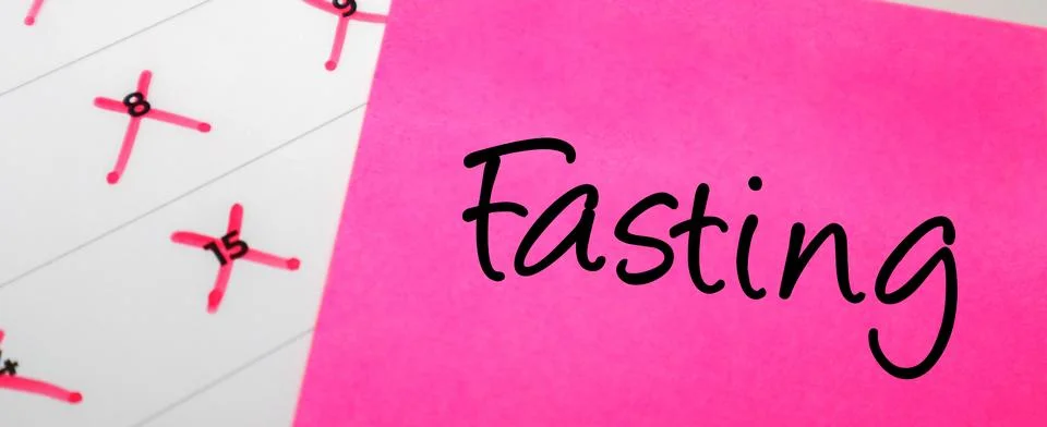 Pink sticky note with Fasting text on a calendar with red marked dates. Con.. Stock Photos