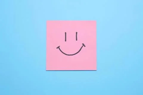 Pink sticky note with a smiley face on blue background Stock Photos