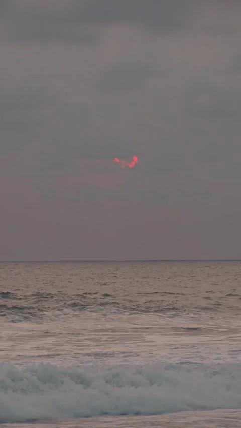 The pink sun slowly setting behind clouds over the ocean horizon 動画素材 343788341