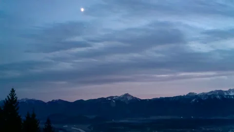 Pink sunset behind the mountains white glowing small moon over the valley Stock Footage 256432604