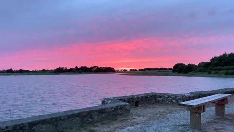 Pink Sunset Sky Over Calm Lake with Stone Wall and Bench Stock Footage 345305319
