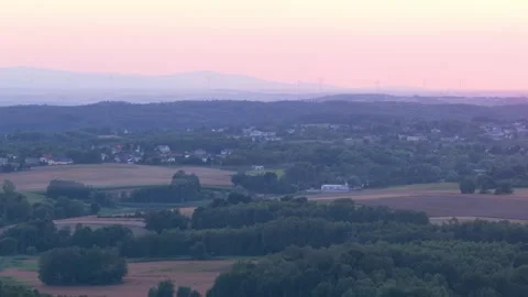 Pink sunset sky over rolling hills and forests with distant wind turbines 스톡 동영상 347874307