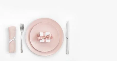 Pink table setting with a gift in a plate, napkin and cutlery on a white Stock Photos