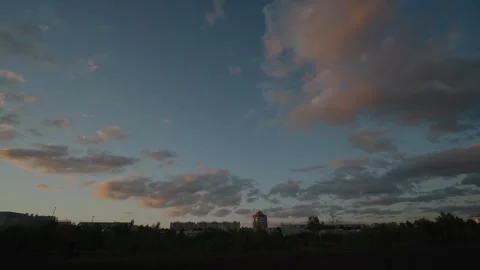 Pink tinged clouds drifting over a dark city skyline at sunset Stock Footage 334627631