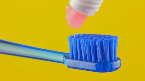 Pink toothpaste is placed on a blue toothbrush on a yellow background close-up. Stock Footage 147167740