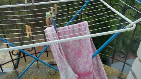 A pink towel hanging on a folding drying rack on the balcony flutters in th.. Vídeos de archivo 329691192