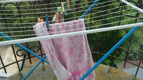 A pink towel hanging on a folding drying rack on the balcony flutters in th.. Vídeos de archivo 335142291