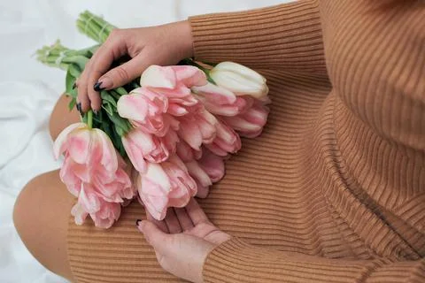 Pink tulips in the hands of a woman. A woman sits on the bed and holds a bouq Stock Photos