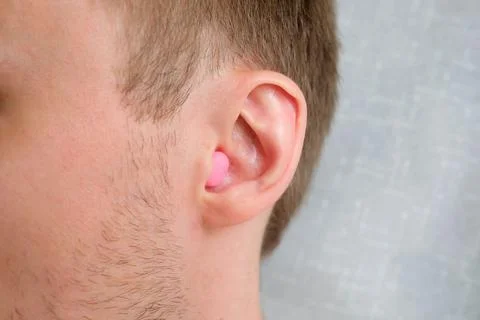 A pink wax earplug is inserted into the ear Stock-Fotos