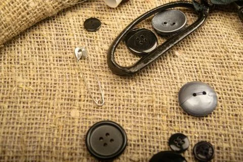 Pins of various sizes, tailor's scissors, and various buttons on coarse-textu Stock Photos