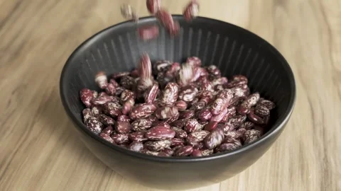 Pinto beans falling into black bowl on wooden table 4k 10bit 120fps Видео 333355008