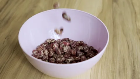 Pinto beans falling into pink bowl on wooden table 4k 10bit 120fps Stock Footage 333414941