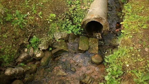 A pipe of a broken water pipe sticking out of the ground. From it flows a stream Stock Footage 76685860