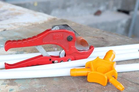Pipe cutters lie on a background of white plastic pipes. Tools Stock Photos