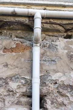 Pipe running along a stone wall with rough texture in a close-up view Stock Photos
