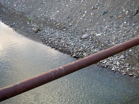 Pipe runs over the river. Rusty pipe.  Pebble bank of the river and sea Foto stock