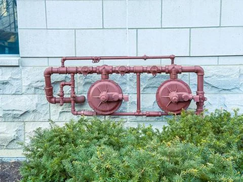 A pipe system is mounted on a wall next to a building. The pipes are painted  Stock Photos