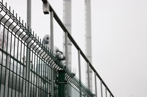 Pipeline and pipeline elements behind metal fence and mesh against gray sky. Stock Photos