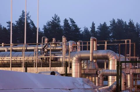 Pipeline and pipeline elements behind a metal fence in the evening close-up. Stock Photos