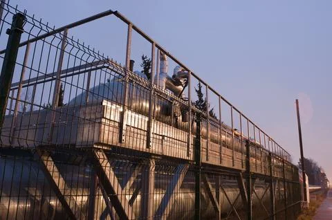 Pipeline and pipeline elements behind a metal fence in the evening close-up. Stock Photos