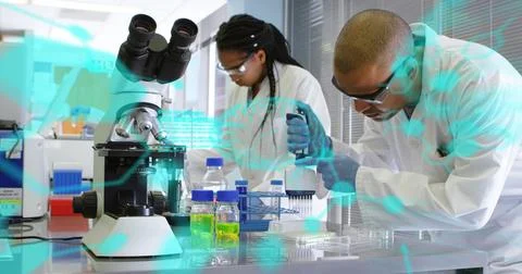 Pipetting tech on right using pipette into plate at bench, with labcoat goggles Stock Photos