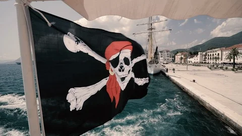A pirate flag flies in the wind of a ship moving away from the marina Stock Footage 115460847