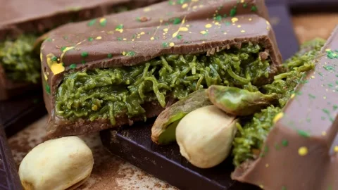 Pistachio nuts falling down on Dubai Chocolate bar with green kadayif Stock Footage 284255161