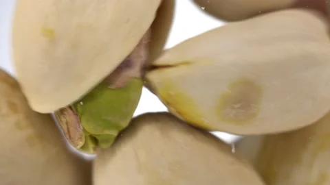 Pistachios in shells fall on glass against a bright white background. Pistachios Stock Footage 148478748
