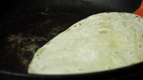 Pita is cooked in a pan, turned over with an orange spatula Stock Footage 129731575