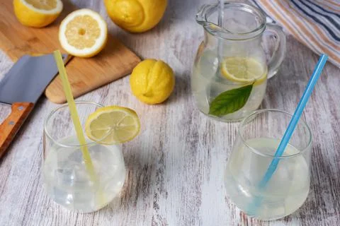 Pitcher and two glasses with lemonade and ice, along with some lemons and a c Stock Photos