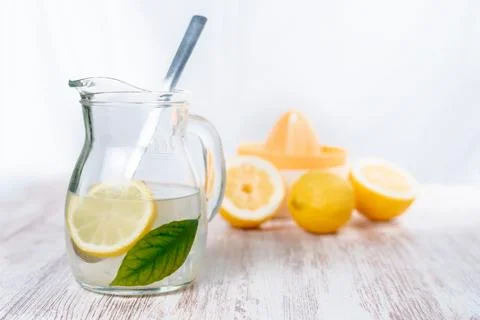 Pitcher with lemonade and cubes, a slice of lemon and a green leaf, in the ba Stock Photos