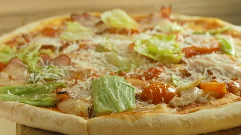 Pizza with bacon, cheese, tomatoes, red onions and leaves, rotating on wooden ba Stock Footage 97300977