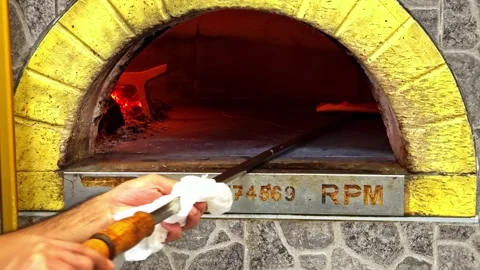 Pizza baking inside traditional stone oven with fire and metal peel tool visible Stock Footage 326281390
