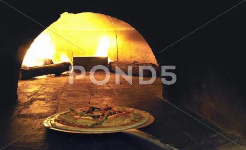 A pizza being placed in a wood-fired oven Stock Photos