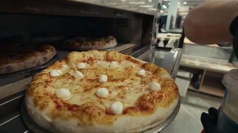Pizza being removed from oven by a worker in a commercial kitchen, showcasing Stock Footage 332736676